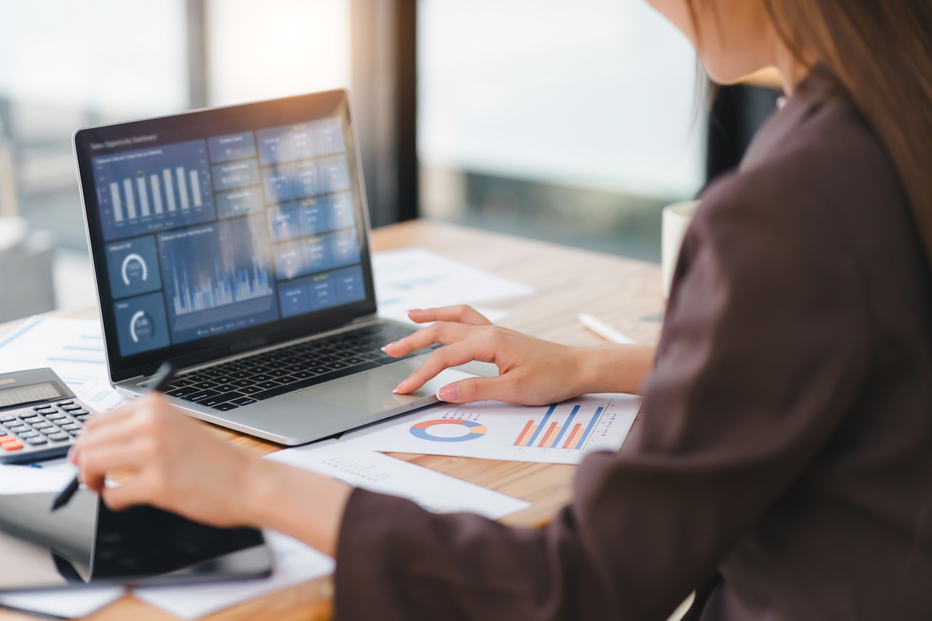 Business professional working on laptop with analytics dashboard, surrounded by financial reports.